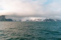 Fjord oświetlony przez słońce, w oddali widać góry i śnieg